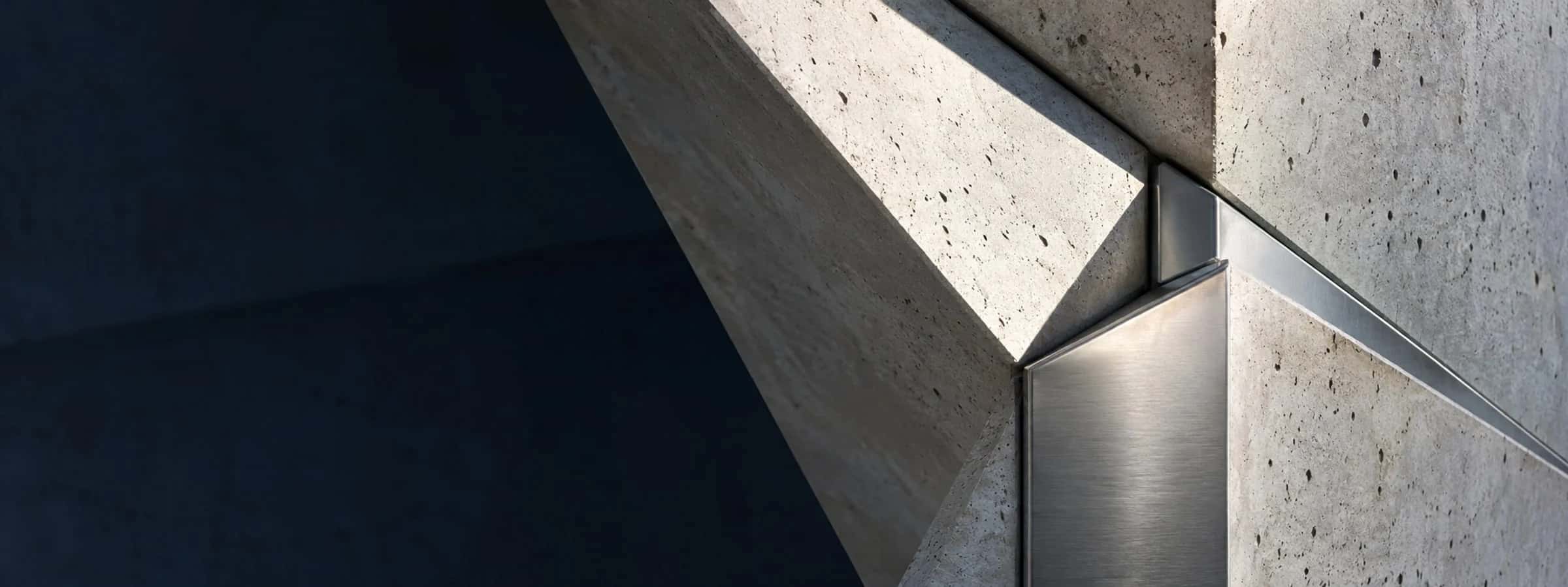 Folded concrete planes and a brushed metal architectural joint in natural light.